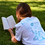 Woman wearing white hotline t-shirt, laying on her stomach and reading a book.