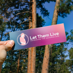 Hand holding bumper sticker with the Let Them Live logo on it.